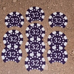 May include: Eight purple and white poker chips with the number 32 printed on each. The chips are arranged in a circle on a brown surface.