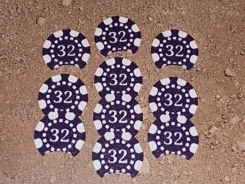 May include: Eight purple and white poker chips with the number 32 printed on each. The chips are arranged in a circle on a brown surface.