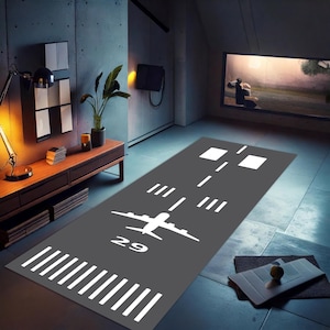 Puede incluir: Una alfombra de pista de aterrizaje de avión gris y blanca con el número 29 impreso en ella. La alfombra está colocada en un suelo de baldosas grises en una habitación con una cómoda de madera y una planta.