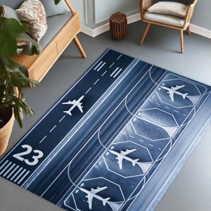 Könnte beinhalten: Ein blauer und weißer Flugzeug-Landebahn-Teppich mit der Nummer 23 darauf gedruckt. Der Teppich zeigt mehrere weiße Flugzeuge in verschiedenen Positionen auf der Landebahn.