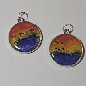 May include: Two circular pendants with a rainbow gradient design, featuring red, orange, yellow, green, and blue hues. One pendant reads "Do you know who you are?" and the other says "Only the brave."