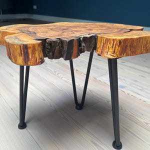 May include: A wooden coffee table with a natural wood finish and a live edge top. The table has three black hairpin legs.