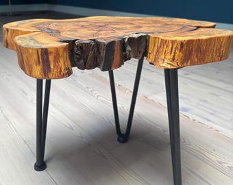 May include: A wooden coffee table with a natural wood finish and a live edge top. The table has three black hairpin legs.
