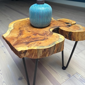 May include: A wooden coffee table with a live edge top and black hairpin legs. A blue and white striped ceramic vase sits on the table.