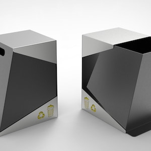 Puede incluir: Dos papeleras modernas y geométricas. Las papeleras son principalmente plateadas y negras, con forma rectangular y diseño inclinado. Cada una tiene un recorte de asa y un símbolo de reciclaje.