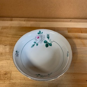 May include: A white ceramic bowl with a green and pink floral design. The bowl has a wide rim and a slightly curved bottom.