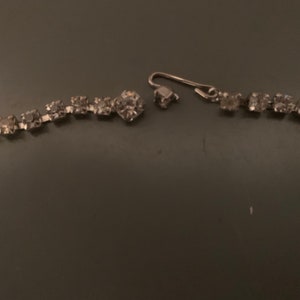 K&ouml;nnte beinhalten: Eine silberne Strasskette mit einem gebrochenen Verschluss. Die Kette besteht aus kleinen, klaren Strasssteinen, die durch silbernes Metall verbunden sind.