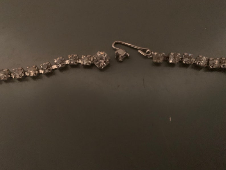 K&ouml;nnte beinhalten: Eine silberne Strasskette mit einem gebrochenen Verschluss. Die Kette besteht aus kleinen, klaren Strasssteinen, die durch silbernes Metall verbunden sind.