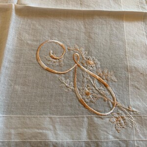 May include: A white cotton handkerchief with an embroidered floral design and the letter "G" in the center.