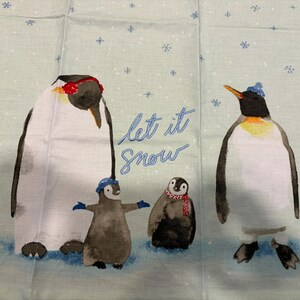 Puede incluir: Tela azul claro con una ilustraci&oacute;n de una familia de ping&uuml;inos. Los ping&uuml;inos llevan gorros y bufandas, con las palabras "Let it Snow" en escritura azul. Los copos de nieve est&aacute;n esparcidos por el fondo.