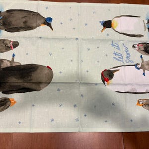Puede incluir: Un pa&ntilde;o de cocina verde claro con un tema invernal. El pa&ntilde;o presenta ilustraciones de ping&uuml;inos con sombreros y orejeras, con las palabras "Let it snow" en escritura azul. Peque&ntilde;os copos de nieve azules est&aacute;n esparcidos por el pa&ntilde;o.