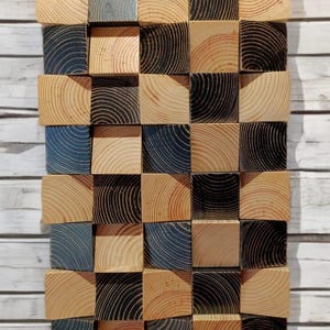 May include: A wall art piece made of wood blocks, with a checkerboard pattern of natural wood and black stained wood. The blocks are arranged in a staggered pattern, creating a three-dimensional effect.