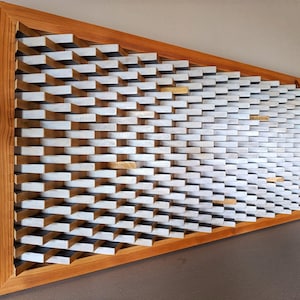 以下が含まれることがあります： 幾何学模様の木製ウォールアート。このアートワークは、三角形の木製フレーム内に配置された、白と自然な木材ブロックのシリーズを特徴としています。ブロックは、視覚的な興味を追加する、テクスチャ加工された3次元効果を生み出します。