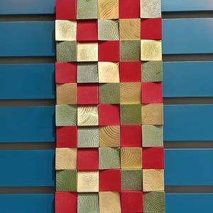 May include: A wall art piece made of wood blocks in a checkerboard pattern. The blocks are painted in shades of red, green, and beige.