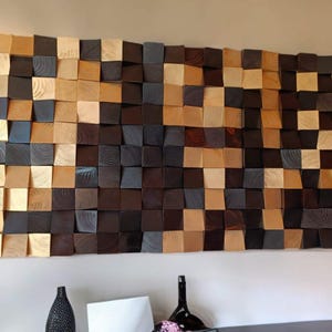Könnte beinhalten: Ein Wandkunstwerk aus Holzblöcken in verschiedenen Brauntönen und Gold. Die Blöcke sind in einem versetzten Muster angeordnet, wodurch ein strukturierter und moderner Look entsteht.