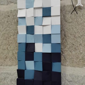 Peut inclure: Une œuvre d'art murale composée de blocs de bois peints dans des tons de bleu, blanc et noir. Les blocs sont disposés en quinconce, créant un effet 3D.