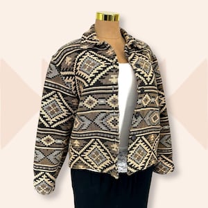 May include: A patterned jacket in shades of brown, black, and beige, displayed on a mannequin. The jacket features a geometric design and a collared neckline. The jacket is open, revealing a white top underneath.