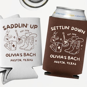 Op de afbeelding: Witte en bruine blikjeskoelers met een western-thema. De witte koeler zegt "Saddlin' Up" en de bruine koeler zegt "Settlin' Down". Beide hebben een gitaar, cowboylaarzen en speelkaarten. De tekst "Olivia's Bach, Austin, Texas" is ook inbegrepen.