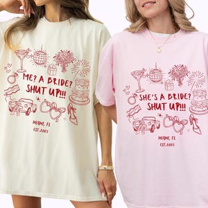 May include: Two t-shirts, one ivory and one pink, with a burgundy design. The design includes wedding-themed illustrations and the text "ME? A BRIDE? SHUT UP!!!" and "SHE'S A BRIDE? SHUT UP!!!", along with "MIAMI, FL EST.2025".