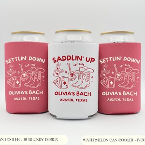 Op de afbeelding: Drie blikjeskoelers, twee in watermeloen en &eacute;&eacute;n in wit, elk met een uniek ontwerp. De ontwerpen omvatten een cowboyhoed, laarzen, een gitaar en speelkaarten. Tekst op de koelers luidt "Settlin' Down" en "Saddlin' Up", met "Olivia's Bach, Austin, Texas".