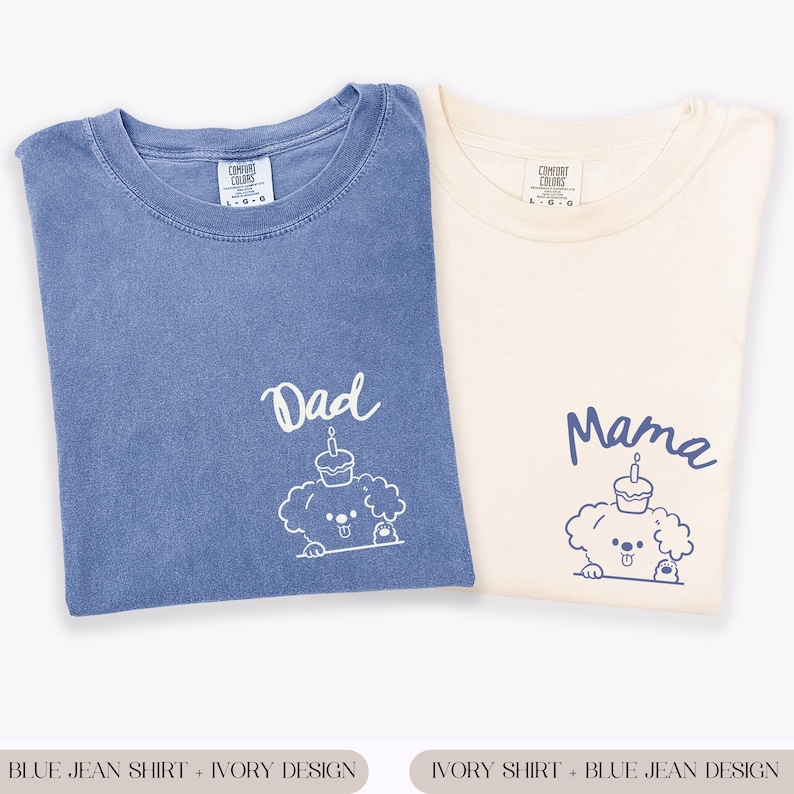 May include: Two Comfort Colors t-shirts, one blue jean and one ivory. The blue shirt has "Dad" and a dog graphic with a cupcake. The ivory shirt has "Mama" and a matching dog graphic. Both shirts are folded.