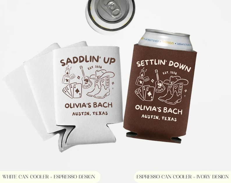 Op de afbeelding: Witte en bruine blikjeskoelers met een western-thema. De witte koeler zegt "Saddlin' Up" en de bruine koeler zegt "Settlin' Down". Beide hebben een gitaar, cowboylaarzen en speelkaarten. De tekst "Olivia's Bach, Austin, Texas" is ook inbegrepen.