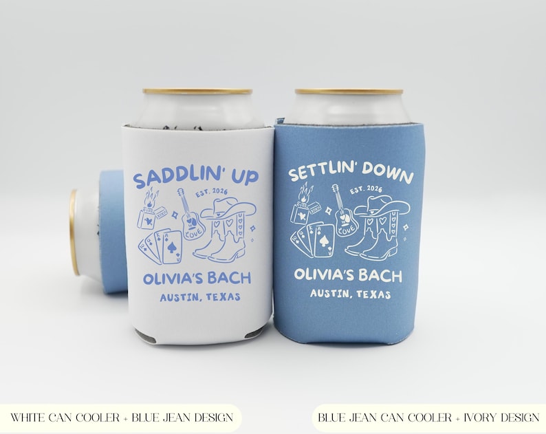 Op de afbeelding: Twee blikjeskoelers, &eacute;&eacute;n wit en &eacute;&eacute;n blauw, met een countrythema. De witte koeler heeft een blauw ontwerp met de tekst "Saddlin' Up", de andere heeft een wit ontwerp met de tekst "Settlin' Down". Beide zeggen "Olivia's Bach, Austin, Texas".