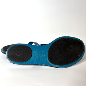 Bottom view of the sandals showing black rubber soles and blue leather trim.