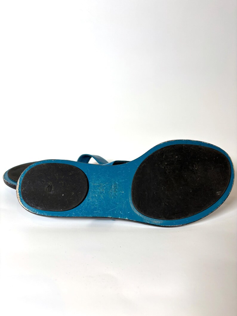 Bottom view of the sandals showing black rubber soles and blue leather trim.