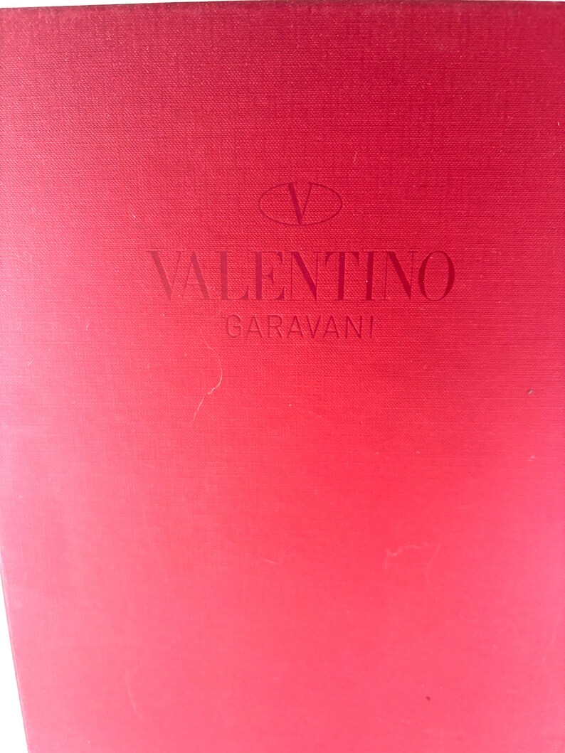 May include: A red box with the Valentino Garavani logo embossed on the front. The logo features a stylized 'V' above the brand name.
