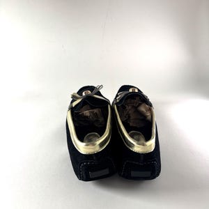 The backs of two black suede loafers with gold trim, showing the heels and the interior lining.
