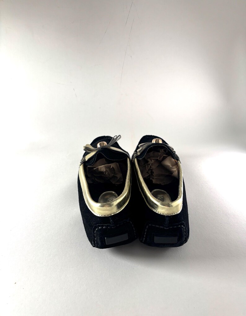 The backs of two black suede loafers with gold trim, showing the heels and the interior lining.