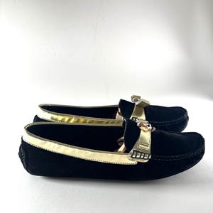 A pair of black suede loafers with gold trim and skull emblems, viewed from the side at a slight angle.