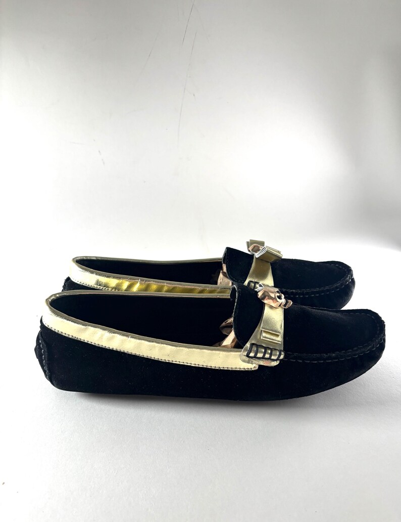 A pair of black suede loafers with gold trim and skull emblems, viewed from the side at a slight angle.