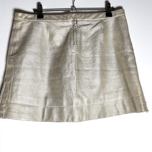 Back view of the cream mini skirt hanging from a black clip hanger, showing a center back zipper and a side zipper at the hem.