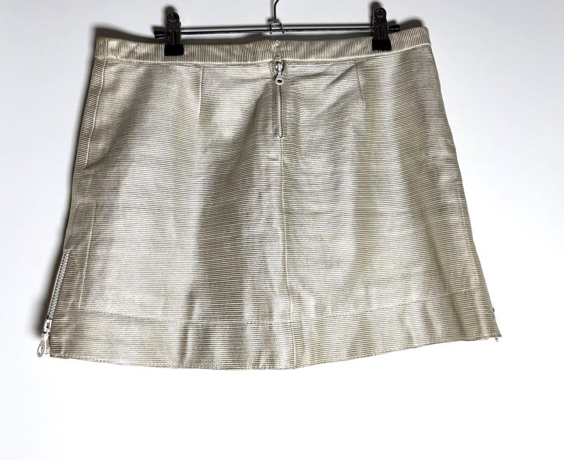 Back view of the cream mini skirt hanging from a black clip hanger, showing a center back zipper and a side zipper at the hem.