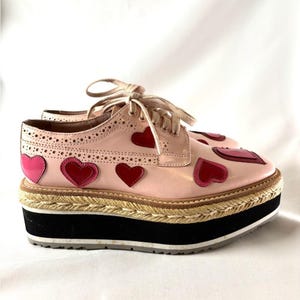 Side profile of a pink platform oxford shoe featuring brogue detailing and multiple contrasting red heart appliques.