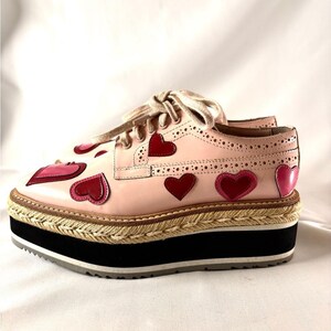 Outer side view of the pink leather platform brogue displaying a row of red and pink hearts along the base.
