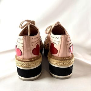 Back view of the platform shoes showing the heel counters decorated with red heart appliques and striped rubber outsoles.