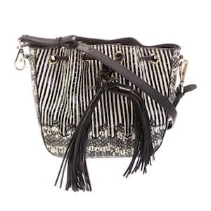 May include: Black and white striped bucket bag with a black shoulder strap and tassels. The bag has gold-tone hardware and a drawstring closure. The bottom of the bag has a snakeskin pattern.