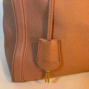 A close-up of a pink leather tag with "ALEXANDER MCQUEEN" embossed on it, hanging from a gold-toned metal piece.