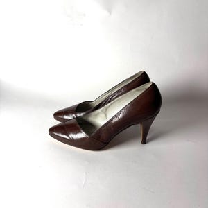 Può includere: Un paio di décolleté in pelle marrone con punta e tacchi a spillo. Le scarpe hanno un design classico e sono su uno sfondo bianco. I tacchi sono alti circa 7,6 cm.