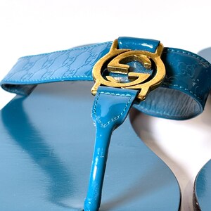Close-up of the blue patent leather strap and gold-tone interlocking G hardware on the sandal.
