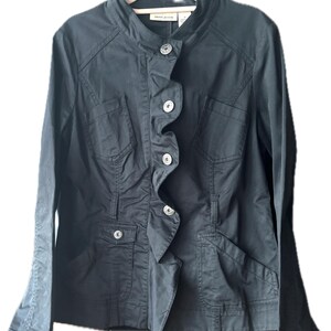 May include: A black long-sleeved jacket featuring a stand-up collar, a vertical ruffled placket, and four silver-toned metal buttons. The jacket includes two chest pockets with flaps and two lower pockets, with the DKNY JEANS label visible at the neck.
