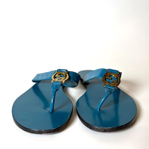 Front view of blue patent leather flat sandals featuring gold-tone interlocking G hardware on a white background.