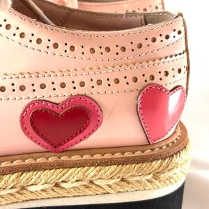 Macro shot focusing on the brogue perforations, stitching, and heart appliques on the upper of the pink shoe.