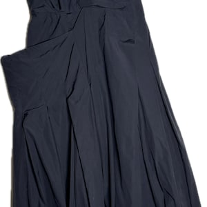 Op de afbeelding: Een strapless zwarte jurk met een getailleerd lijfje en een uitlopende rok. De jurk heeft een gedrapeerd ontwerp op het lijfje en een geplooide rok. De jurk hangt aan een hanger tegen een witte achtergrond.