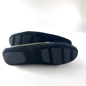 The black rubber soles of two black suede loafers, showing textured grips and a circular logo on one heel.