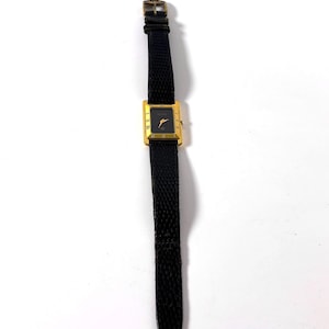 Puede incluir: Reloj de pulsera rectangular dorado con esfera negra y correa de cuero negro. El reloj tiene números romanos y agujas doradas. La correa es texturizada y tiene una hebilla dorada. Un accesorio clásico.