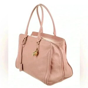 A pink leather handbag with two top handles and a gold skull charm, shown from a three-quarter view on a white background.